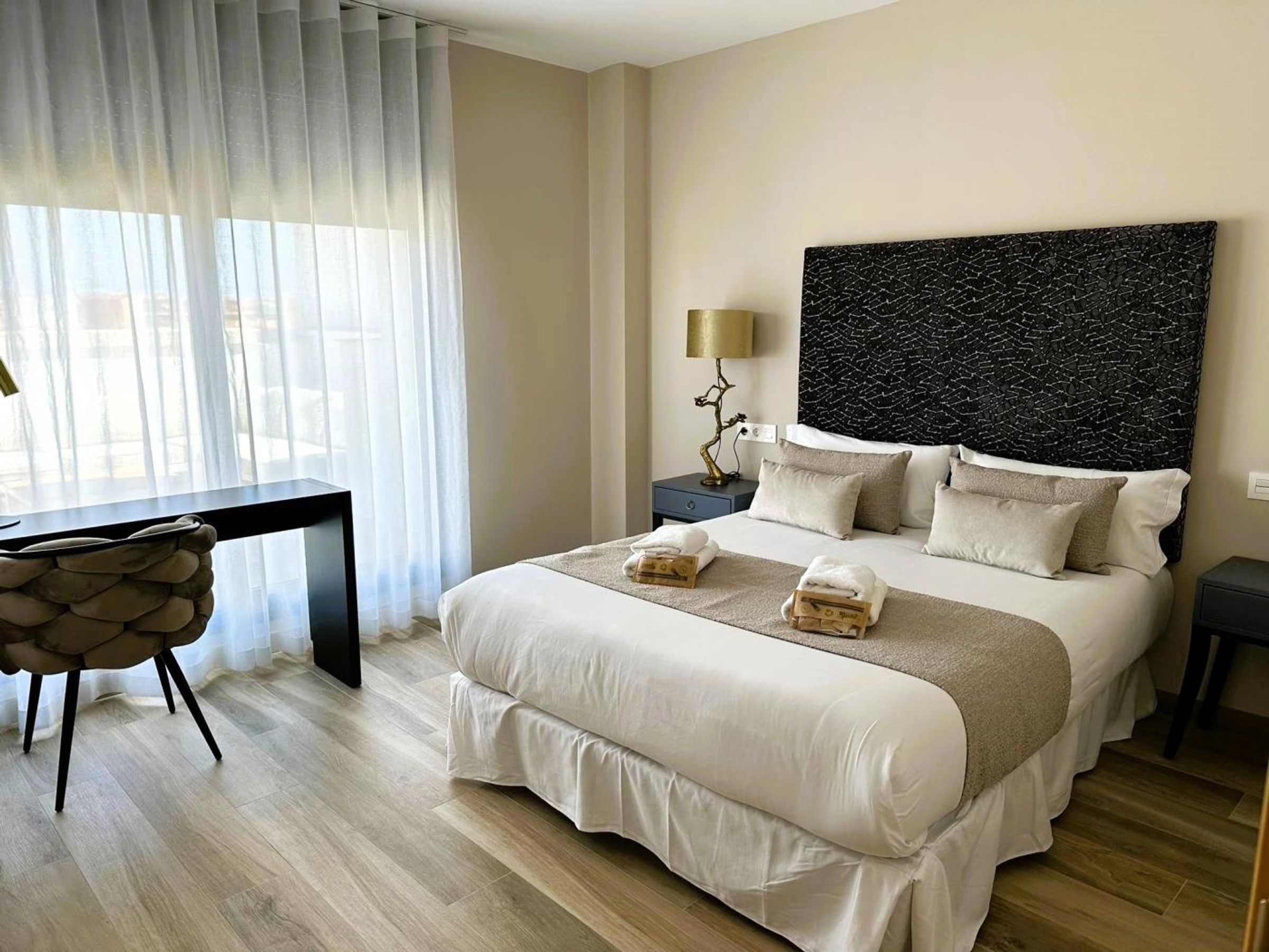 Ett hotellrum med en stor säng, ett skrivbord, en stol, en lampa och en dekorativ väggdekoration.