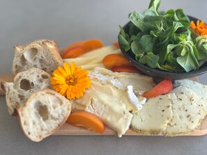 Una tabla de madera con queso, pan y un bol de verduras.