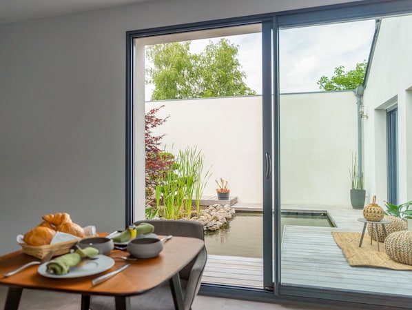 A dining area with a table set for two, a sliding glass door leading to an outdoor patio with a small pond and potted plants.