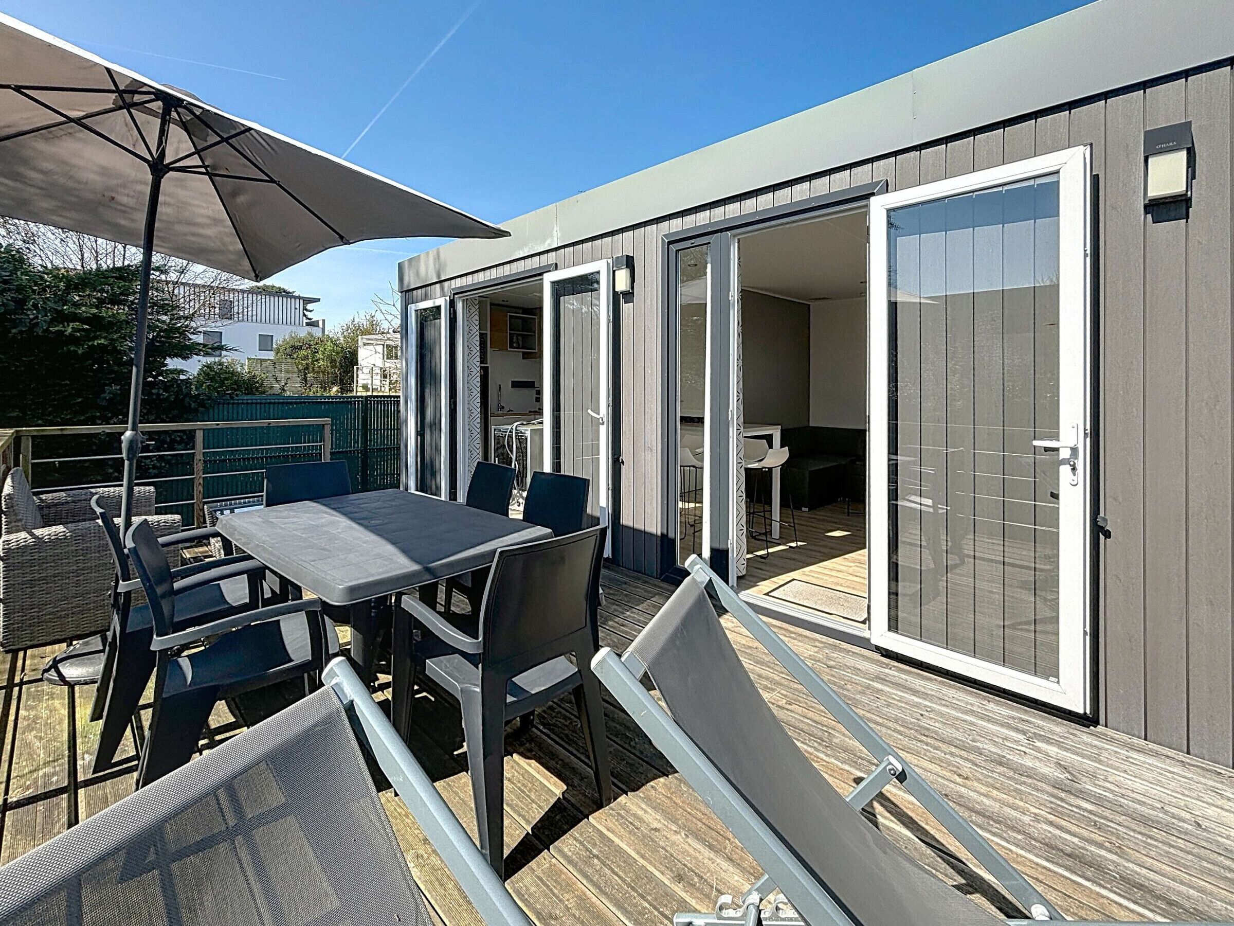 A modern outdoor patio with a table and chairs, a large umbrella, and a sliding glass door leading to an interior space.