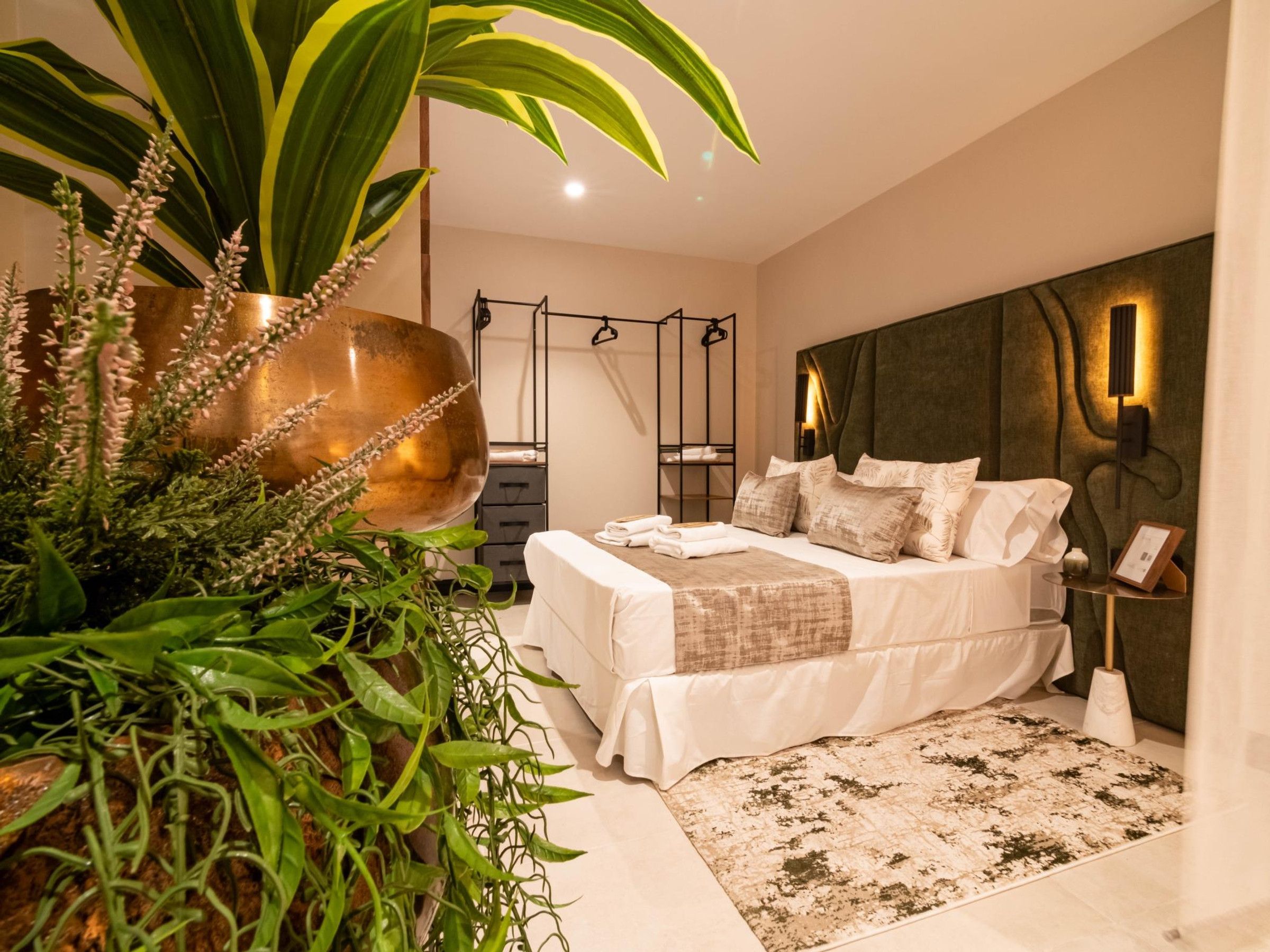 Un dormitorio moderno con cama, mesita de noche y una gran planta en maceta.