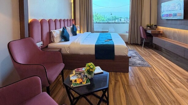 A modern hotel room with a bed, seating area, TV, and a view of the outdoors. - Infinity Hotel (Kanpur)