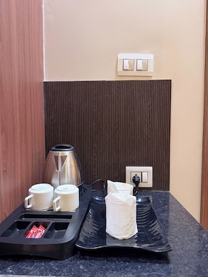 Una kitchenette con una cafetera, dos tazas blancas, una bandeja negra y una caja de pañuelos.