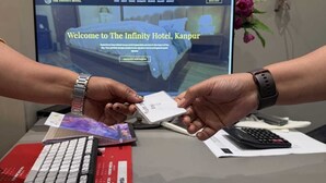 A hotel reception desk with a computer displaying the Infinity Hotel's website, a keyboard, a calculator, and a card being exchanged. - Infinity Hotel (Kanpur)