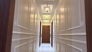 A long, narrow hallway with white paneled walls and a reflective floor, leading to a wooden door at the end. - Infinity Hotel (Kanpur)