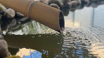 Un tuyau en bambou déverse de l’eau dans un bassin entouré de rochers.