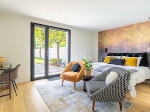 A modern bedroom with a bed, a desk, and a chair. There is a sliding glass door leading to an outdoor area with trees. - Spacious room with terrace and pool (SUCE-SUR-ERDRE)