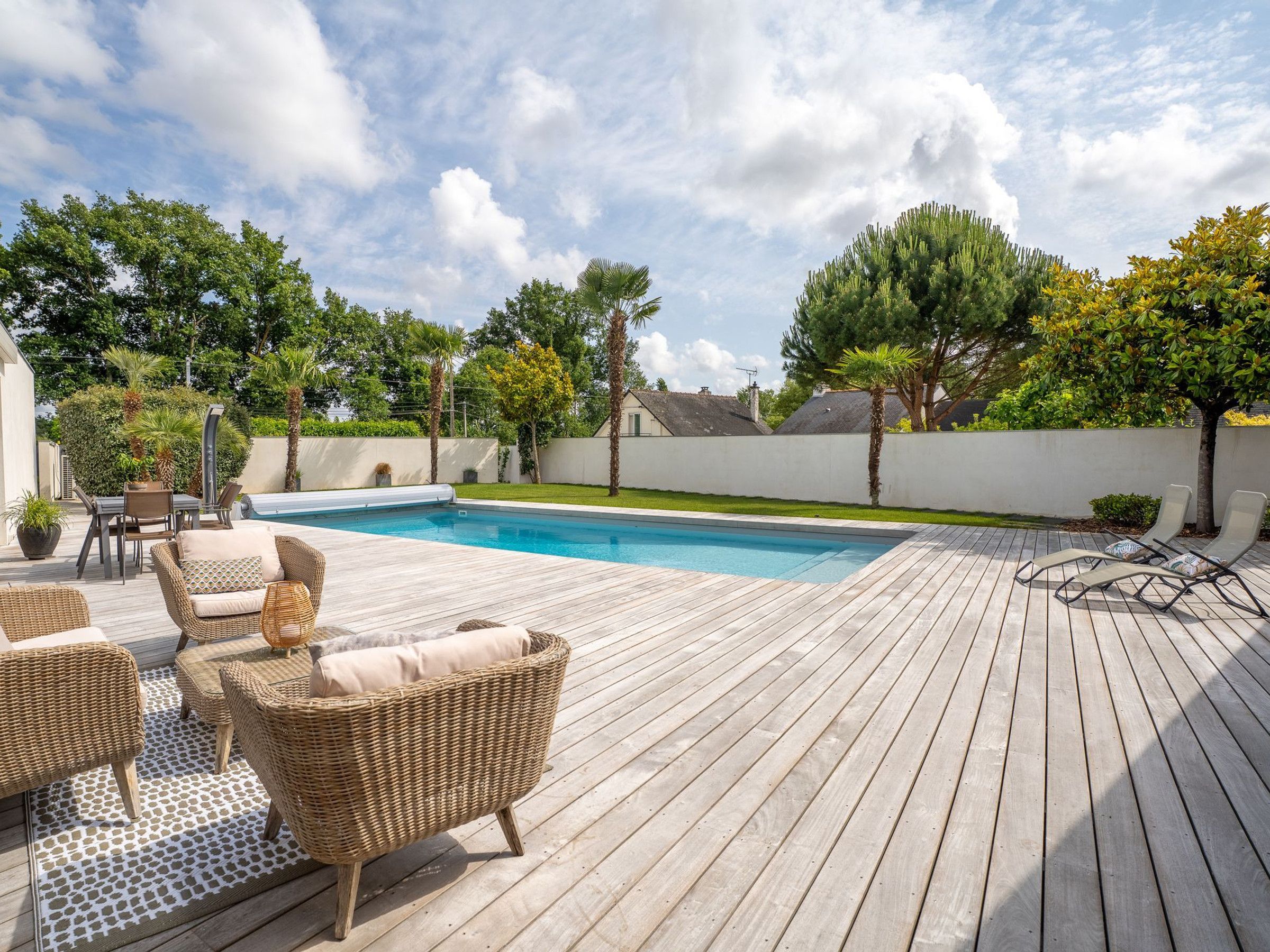 Une terrasse en bois avec une piscine, des meubles en osier et des arbres.