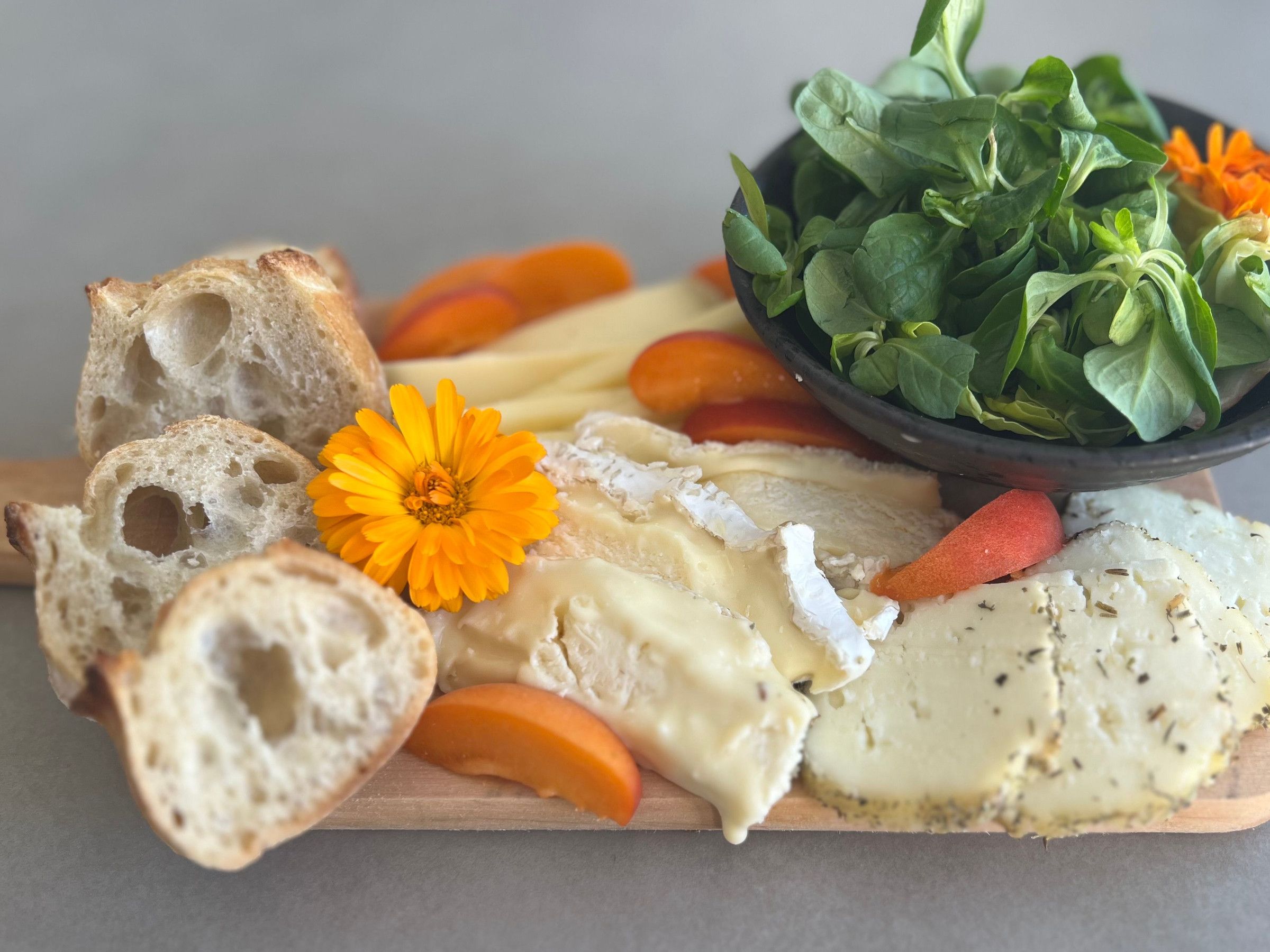 Una tabla de madera con queso, pan y un bol de verduras.