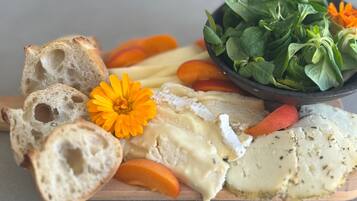 Una tabla de madera con queso, pan y un bol de verduras.