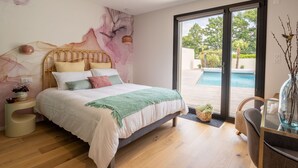 A bedroom with a bed, a nightstand, a chair, a table, and a view of an outdoor swimming pool. - Ground floor room with terrace (SUCE-SUR-ERDRE)