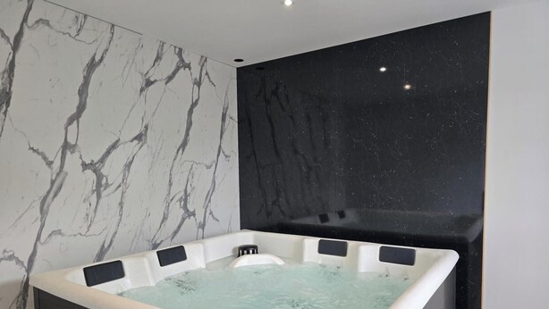 Une salle de bain moderne avec un mur en marbre, un mur d’accent en marbre noir et une baignoire sur pieds.