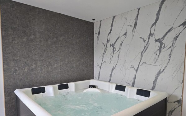 Un baño moderno con pared de mármol, bañera con múltiples jets y un taburete pequeño.