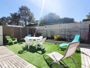 Un patio trasero con césped artificial, una terraza de madera y una zona cercada.