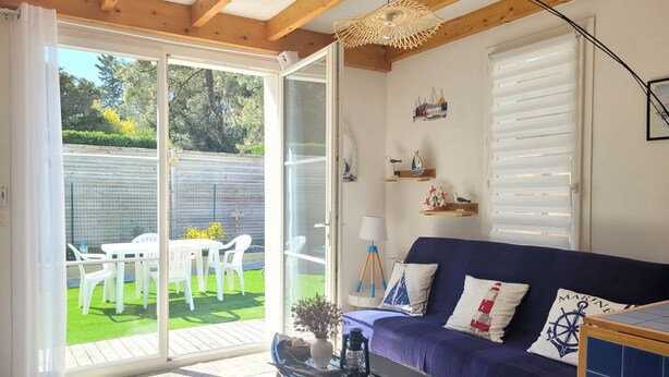 Una habitación con un sofá azul, una mesita con un farol y vistas a un jardín a través de una puerta corrediza de vidrio.