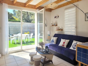 A room with a blue sofa, a small table with a lantern, and a view of a garden through a sliding glass door.
