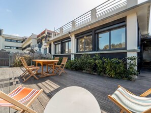Un patio exterior moderno con una mesa y sillas de madera, una pequeña mesa redonda y una terraza de madera.
