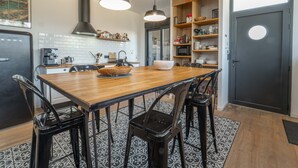 Cocina moderna con una mesa de madera, sillas negras, lámparas colgantes y un refrigerador negro.