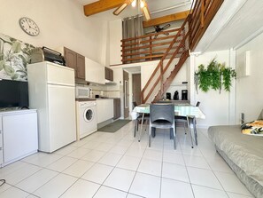 Eine kleine Küche mit Waschmaschine, einem Esstisch mit Stühlen, einer Treppe und einem Bett.