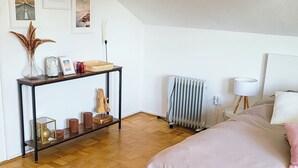 Et soveværelse med trægulv, en hvid seng, et natbord, en radiator og en væg med billeder i rammer.
