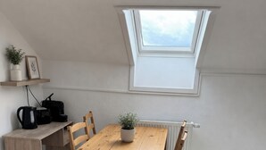 Et værelse med et træbord, stole, en lille potteplante, en radiator og et ovenlys.