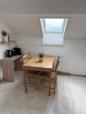 Een kamer met een houten eettafel, stoelen, een kleine potplant, een radiator en een dakraam.