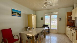 A room with a dining table, chairs, a ceiling fan, a window with a view, and a kitchen area. - House near sea, sunny terrace - 6 guests (Saint-Hilaire-de-Riez)