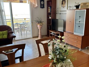 A living room with a TV, wooden furniture, a dining table, and a potted plant. - Apartment with stunning view - 4 guests (La Pineda)