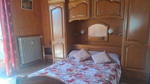 Une chambre à coucher avec une tête de lit en bois, un lit recouvert d’une couvre-lit à motifs, deux oreillers, une table de chevet et un miroir au-dessus du lit.