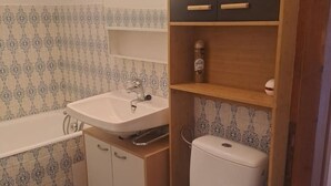 Une salle de bain avec un lavabo blanc, une baignoire, des toilettes et des meubles en bois.