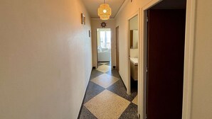 Un couloir avec un sol à carreaux, un luminaire suspendu et une porte donnant sur une salle de bain.