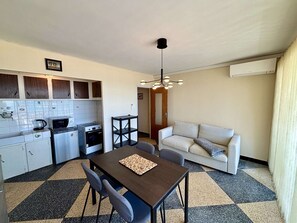 A compact kitchen with a dining table and chairs, a sofa, and a ceiling light fixture. - Apartment sea view with AC - 4 guests (Port-la-Nouvelle)