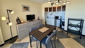 Un espace de vie compact comprenant un coin repas, une kitchenette et un téléviseur posé sur un meuble en bois.