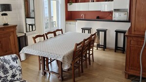Un coin repas avec une table et des chaises, une cuisine avec des meubles blancs et une fenêtre avec des rideaux.
