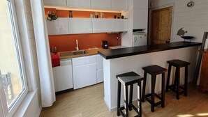 Une cuisine compacte avec des meubles blancs, un plan de travail en bois et un petit îlot central doté de tabourets.