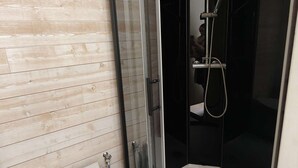 Une salle de bain moderne avec un mur en bois, une cabine de douche en verre et un lavabo blanc.
