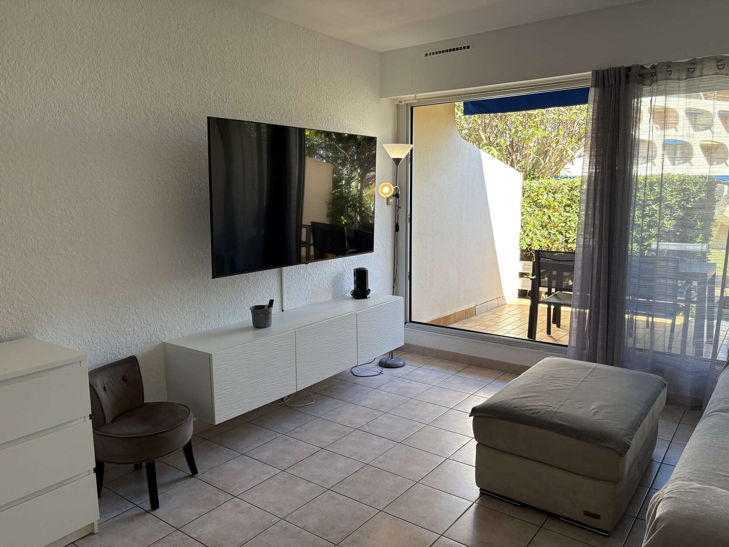 A modern living room with a flat-screen TV, a white console, a cushioned bench, and a sliding glass door leading to an outdoor area.