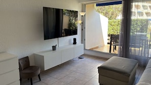 A modern living room with a flat-screen TV, a white console, a cushioned bench, and a sliding glass door leading to an outdoor area.