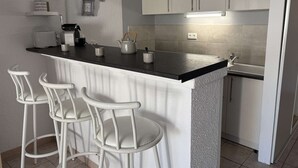 A kitchen with a bar area, white bar stools, and a countertop with various items.