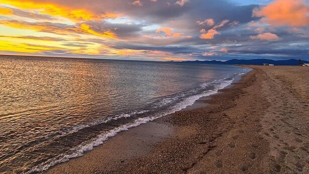 Uma praia com mar calmo, céu claro e montanhas ao longe.