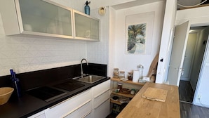 Une cuisine avec un plan de travail noir, des placards blancs, une table en bois et une étagère murale où sont rangés des bocaux.
