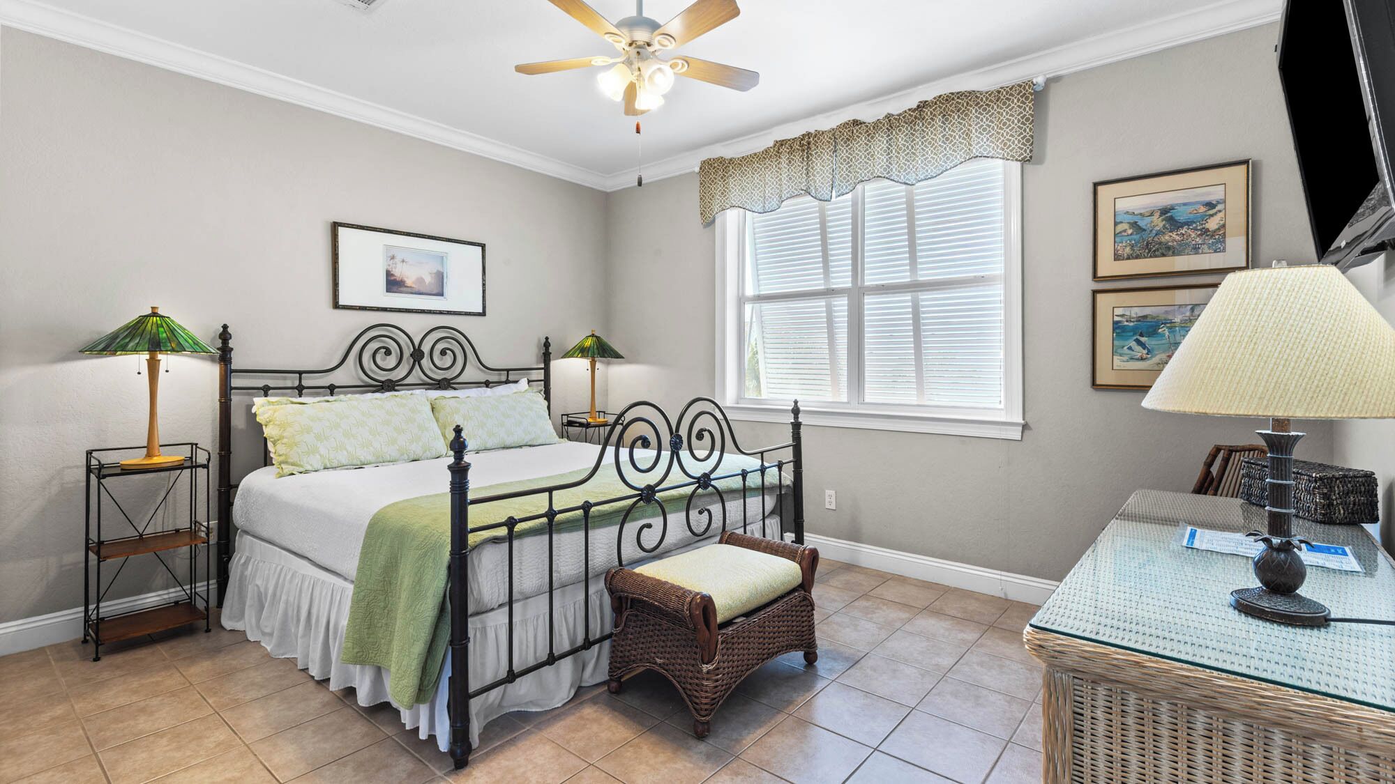 A bedroom with a bed, two bedside tables with lamps, a chair, a window with blinds, and a ceiling fan.