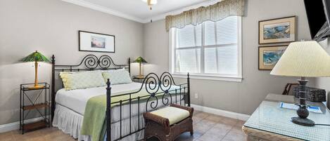 A bedroom with a bed, two bedside tables with lamps, a chair, a window with blinds, and a ceiling fan.