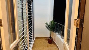 A narrow corridor with a potted plant, a window with blinds, and a door. - Ramatva Stays (Varanasi)