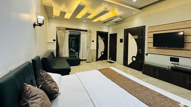 A modern hotel room with a large bed, a TV, a seating area, and a door leading to another room. - Ramatva Stays (Varanasi)