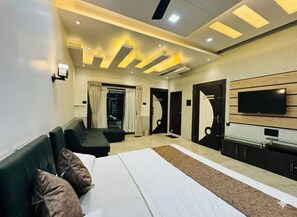 A modern hotel room with a large bed, a TV, a seating area, and a door leading to another room. - Ramatva Stays (Varanasi)