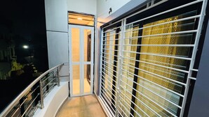 A balcony with a metal railing, a door leading to an interior space, and a window with a metal grid. - Ramatva Stays (Varanasi)