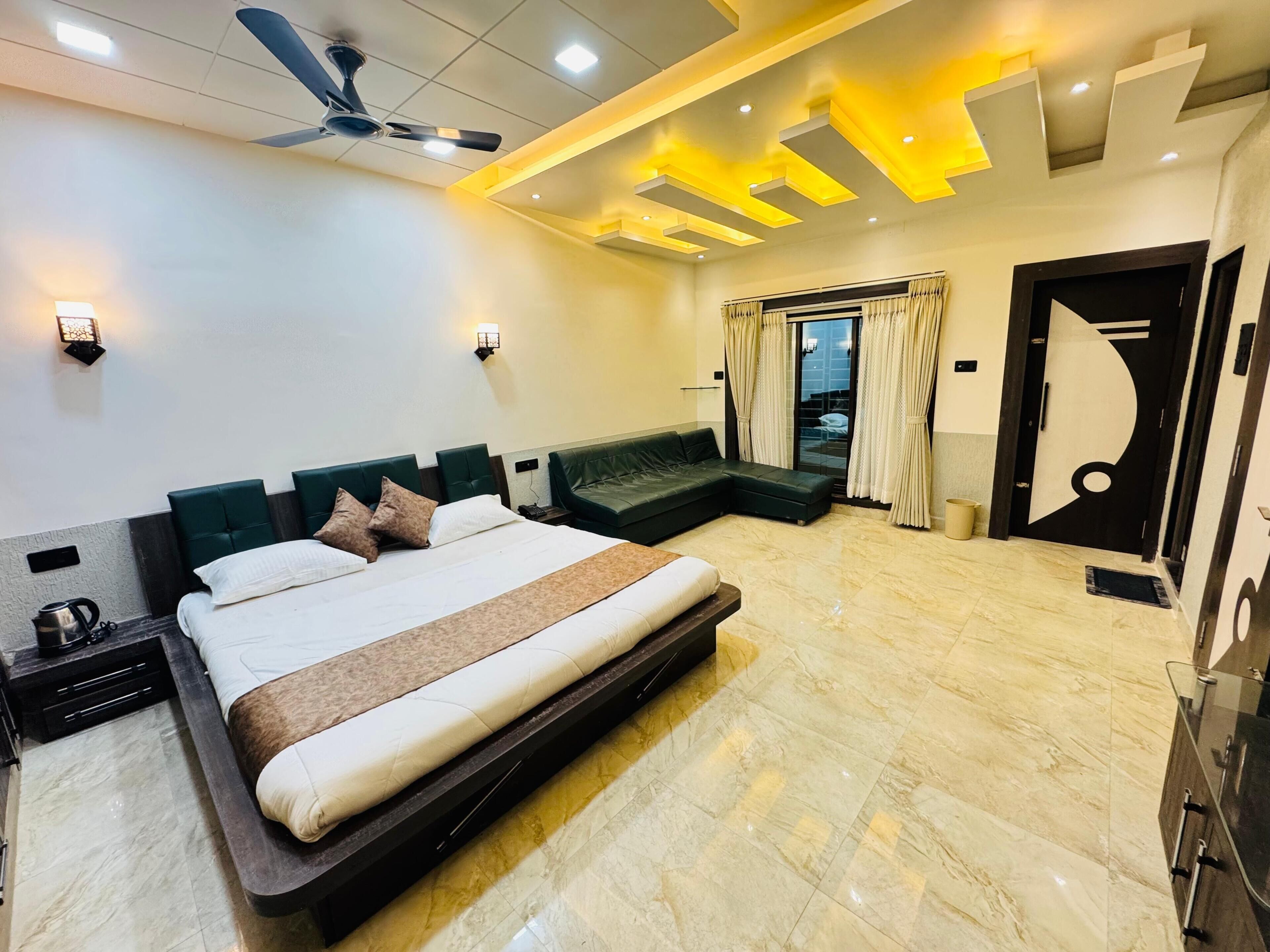 Una habitación de hotel moderna con una cama grande, ventilador de techo, iluminación empotrada y vistas al exterior a través de un ventanal.