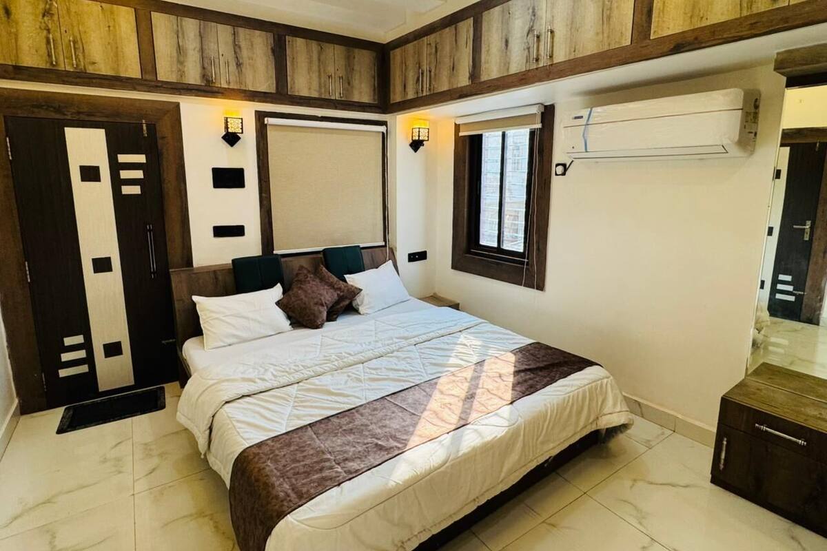 A bedroom with a bed, a wardrobe, a window, and an air conditioning unit.