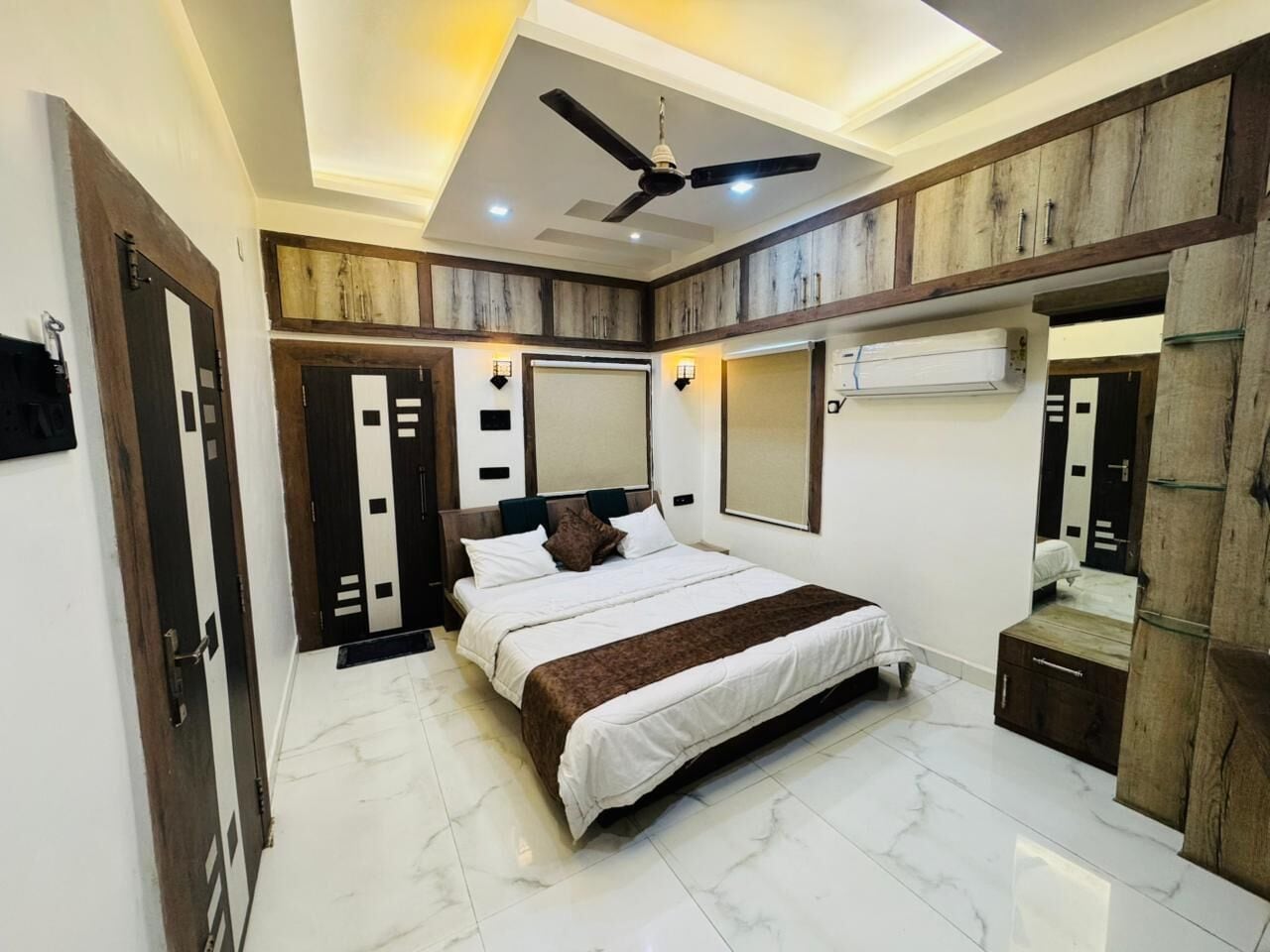 Une chambre à coucher avec un lit, un ventilateur de plafond, une armoire et un miroir.